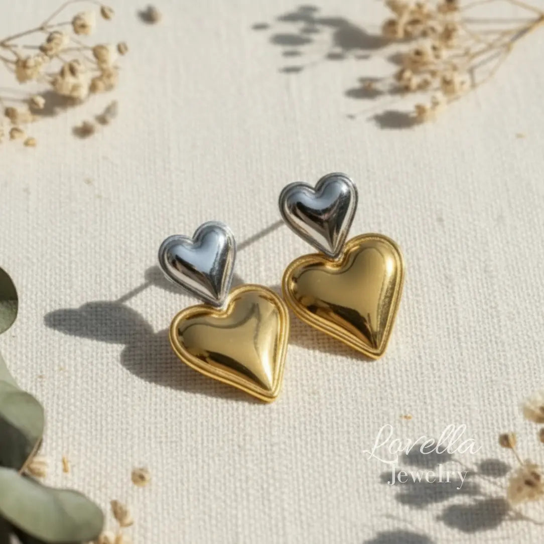 Heart-shaped earrings in gold and silver on a textured surface with 'Lovella Jewelry' branding.