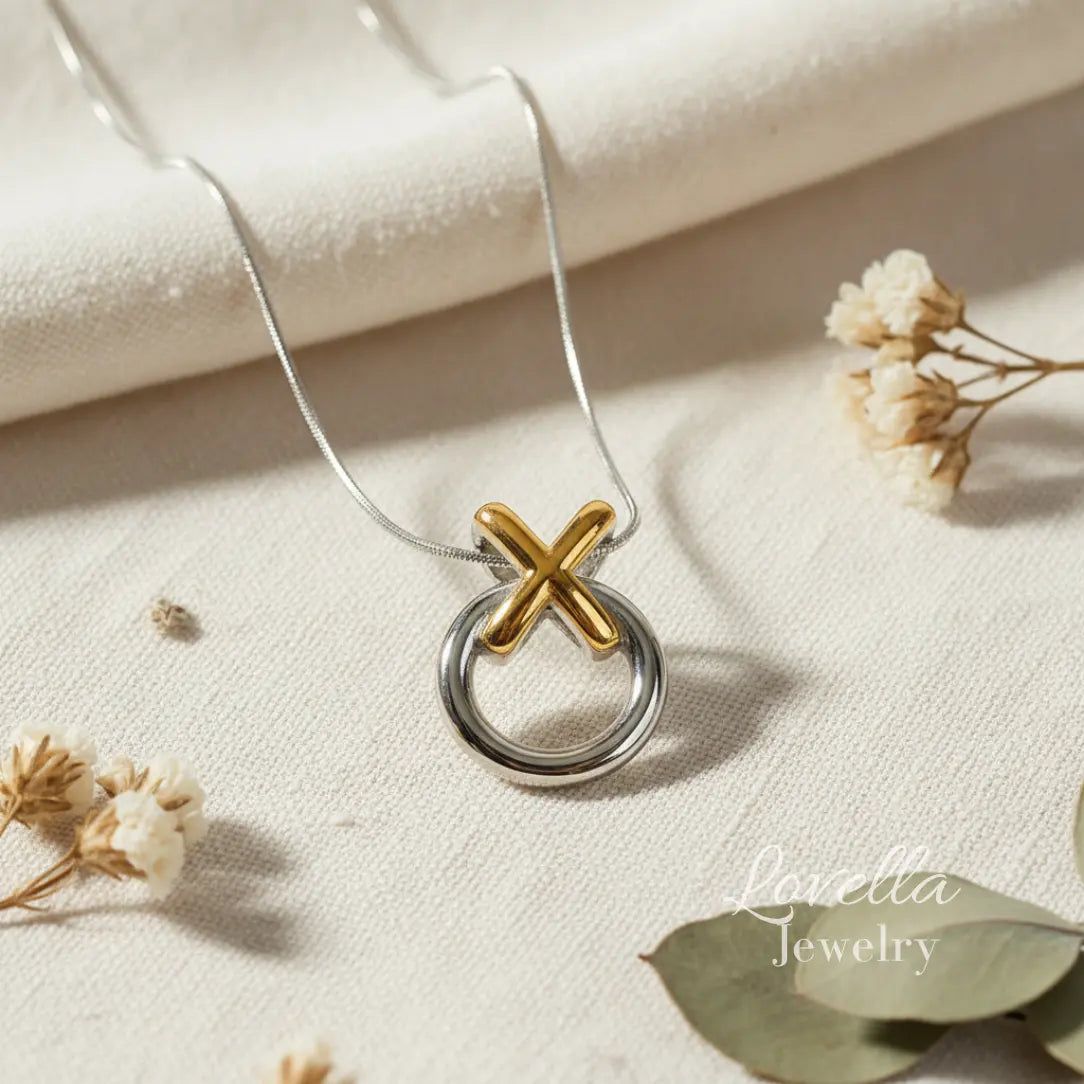 Necklace with a gold and silver pendant on a light fabric background with dried flowers.