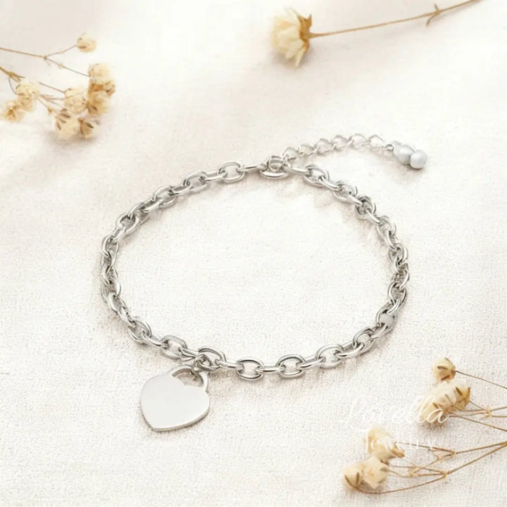 Silver chain bracelet with a heart charm on a light background with dried flowers.