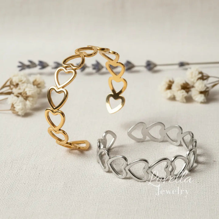 Gold and silver heart-shaped bracelets on a light background with dried flowers.