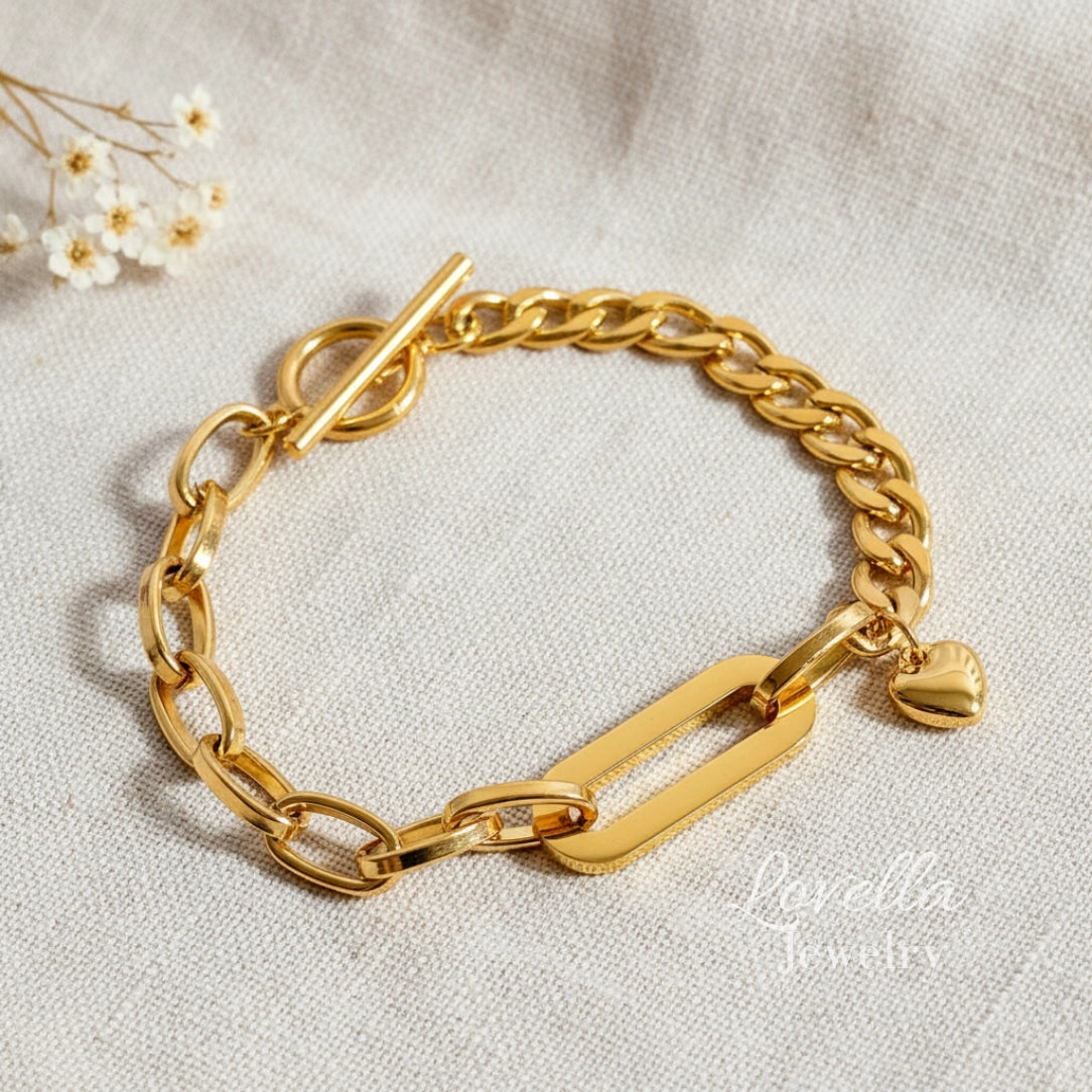 Gold chain bracelet with a heart charm on a light fabric background