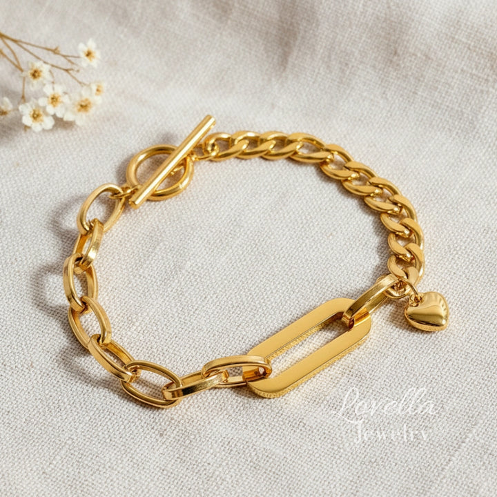 Gold chain bracelet with a heart charm on a light fabric background