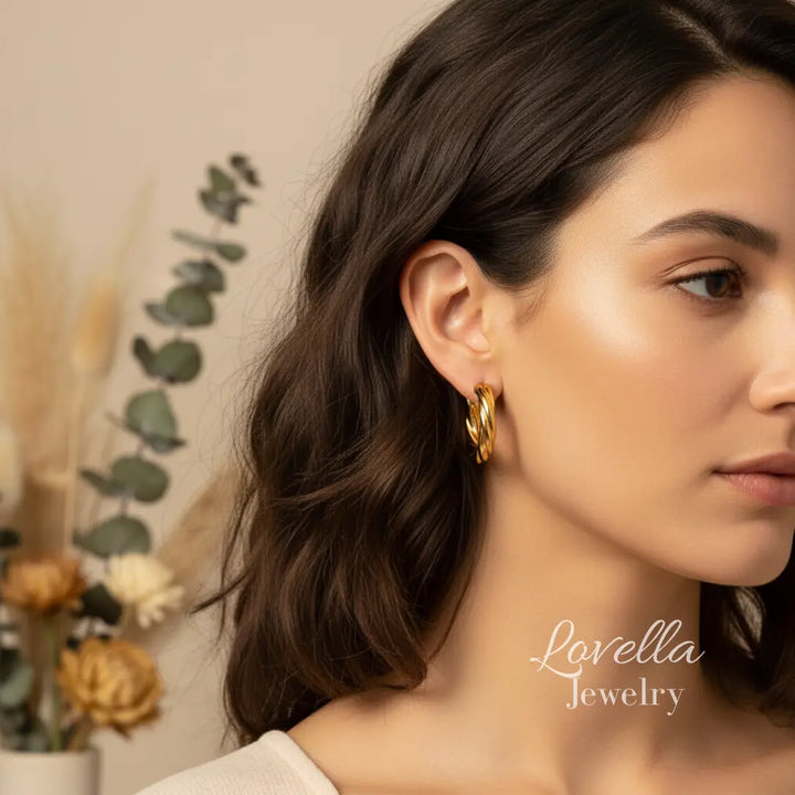 Woman wearing gold hoop earrings with a blurred background and 'Lovella Jewelry' branding.