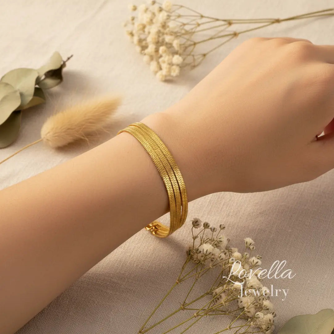 Gold bracelet on a wrist with dried flowers and greenery on a neutral background, featuring Lovella Jewelry.
