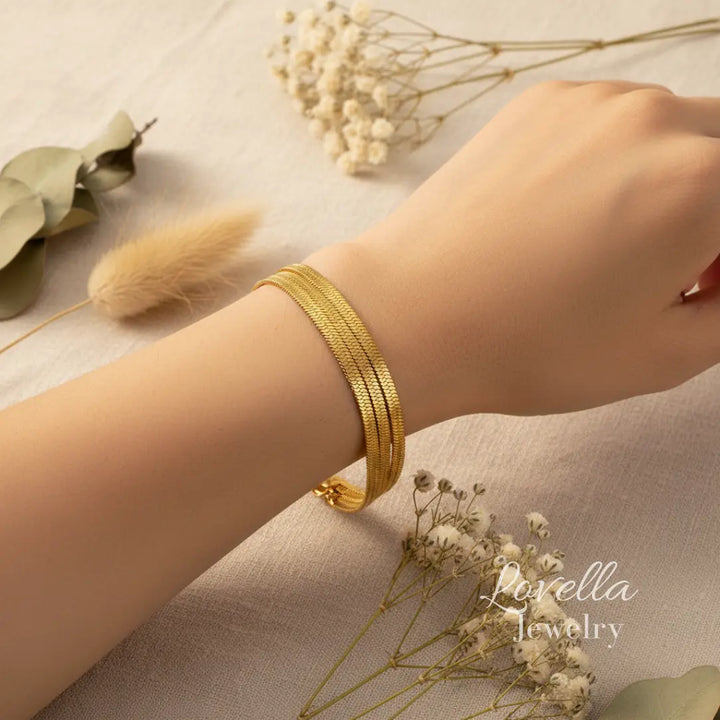 Gold bracelet on a wrist with dried flowers and greenery on a neutral background, featuring Lovella Jewelry.
