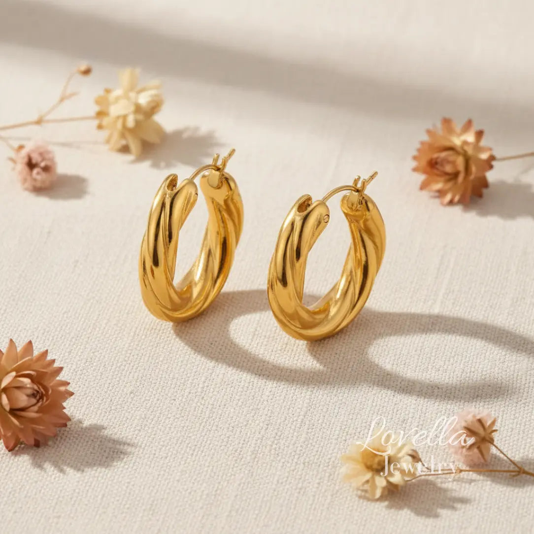 Gold hoop earrings on a light beige fabric background with dried flowers.
