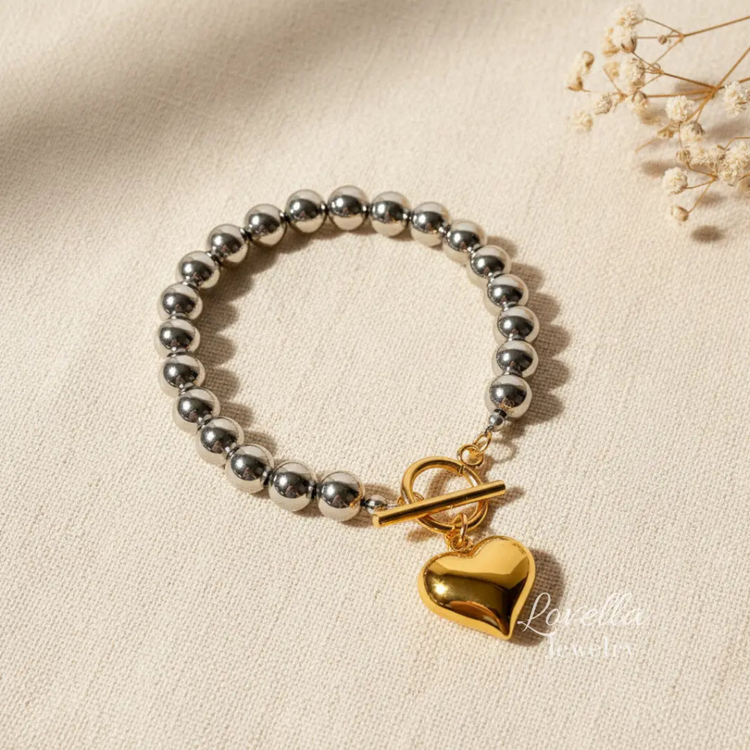 Bracelet with silver beads and a gold heart charm on a beige background