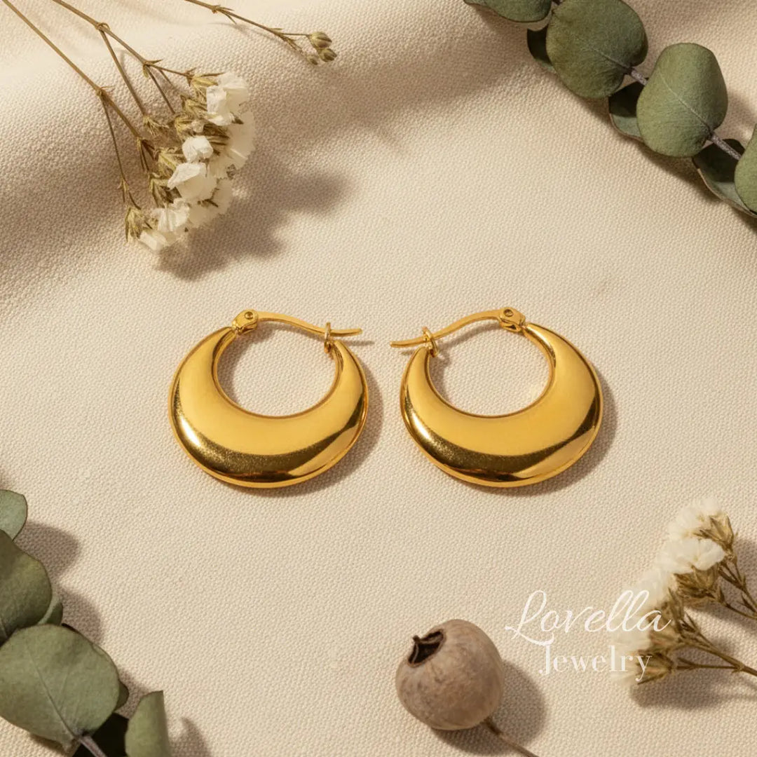 Gold hoop earrings on a beige surface with greenery and flowers.