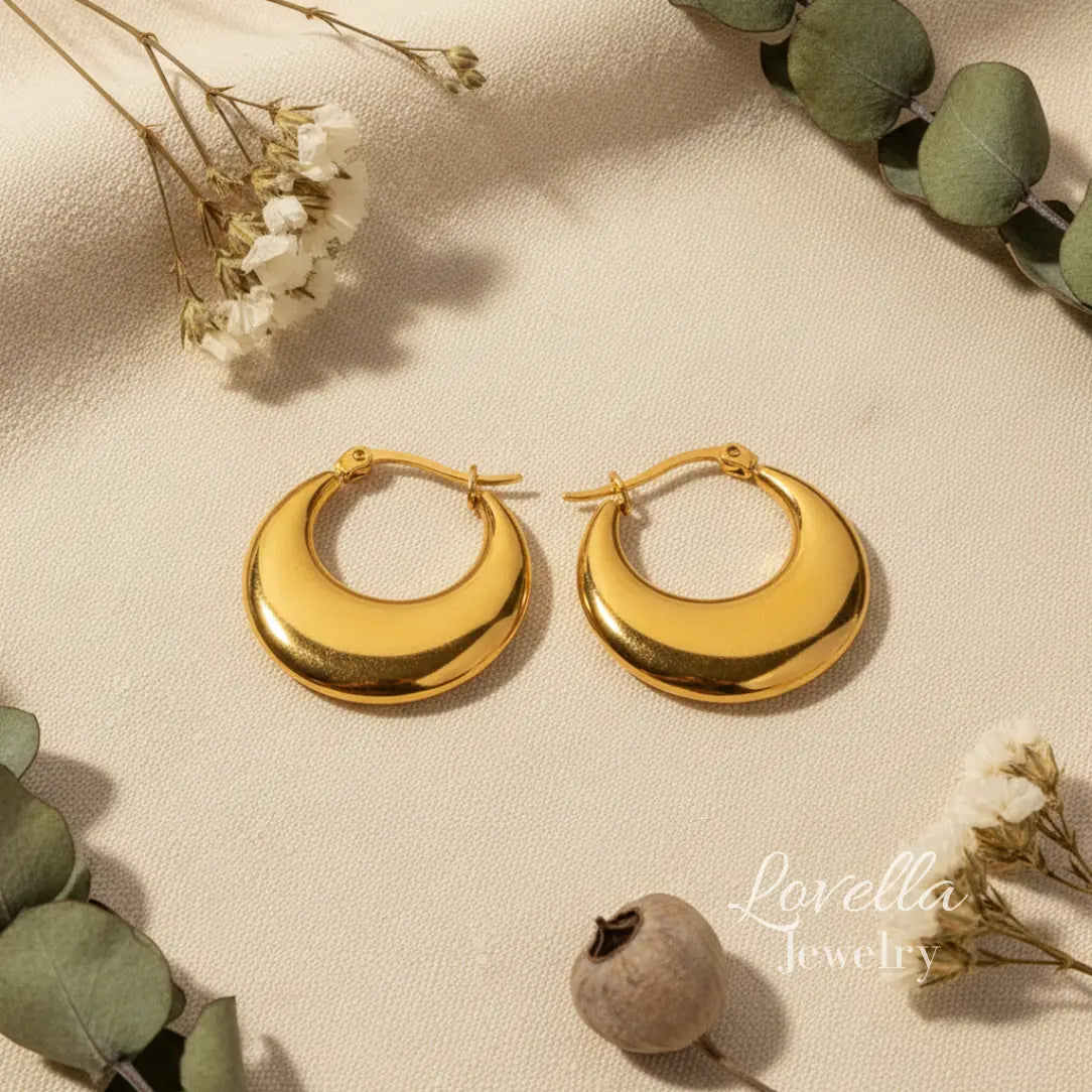 Gold hoop earrings on a beige surface with greenery and flowers.