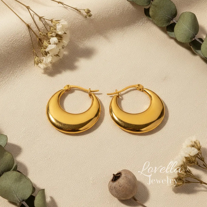 Gold hoop earrings on a beige surface with greenery and flowers.