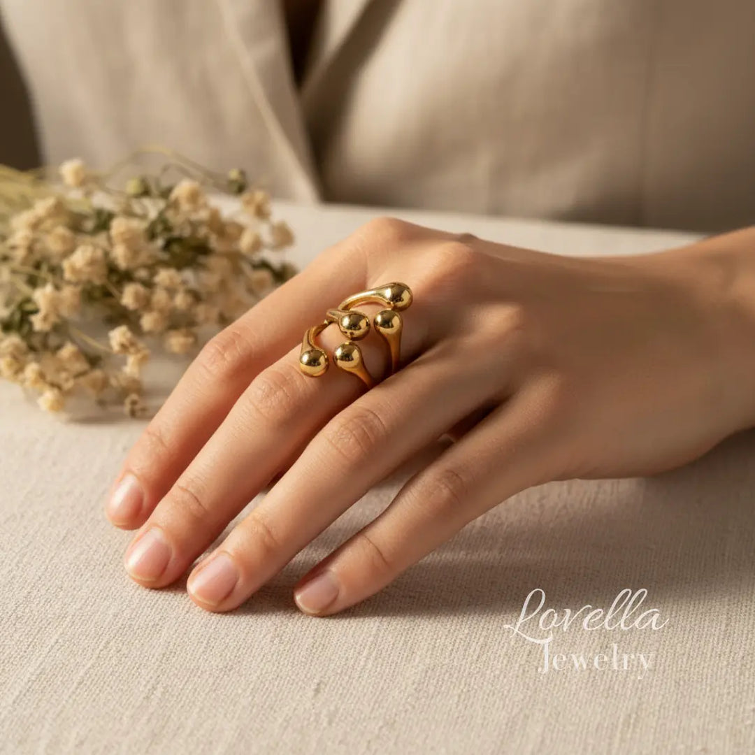 Model wearing a gold-tone stainless steel bubble ring with rounded bead details, shown on hand in warm natural light.