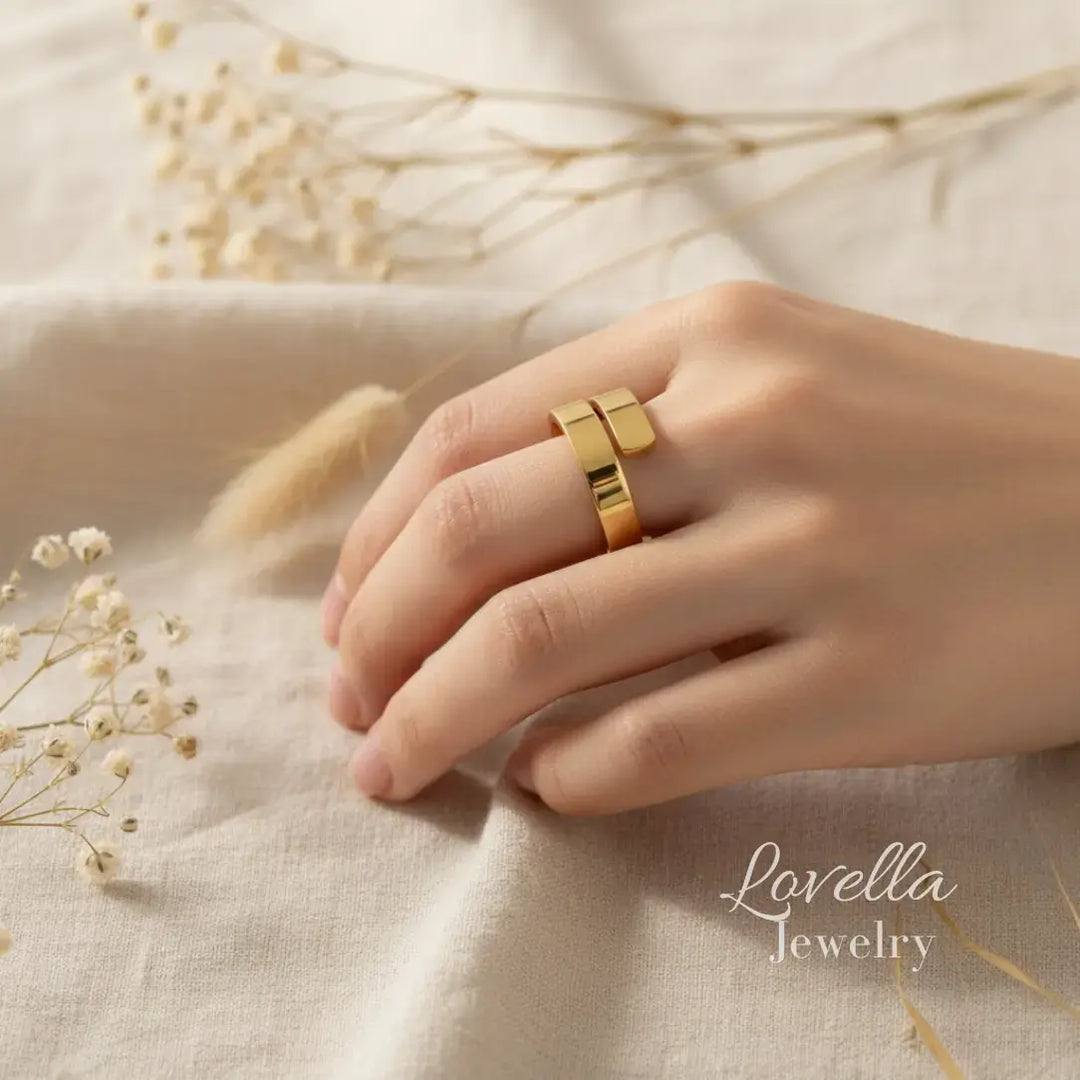 Gold ring on a hand with dried flowers on a beige fabric background, Lovella Jewelry branding visible.