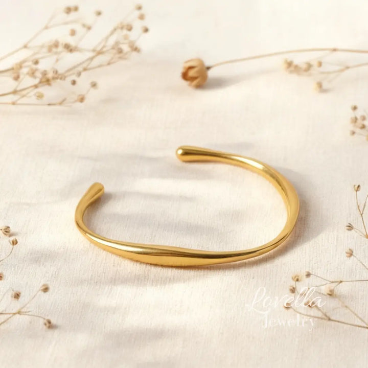 Gold bracelet on a light fabric background with dried flowers
