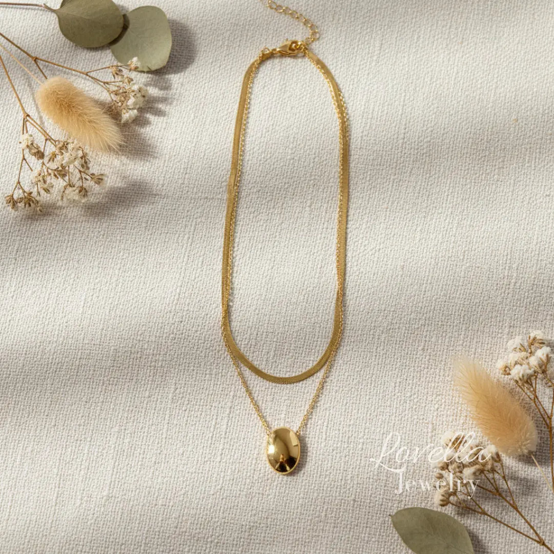 Gold necklace on a textured beige surface with dried flowers