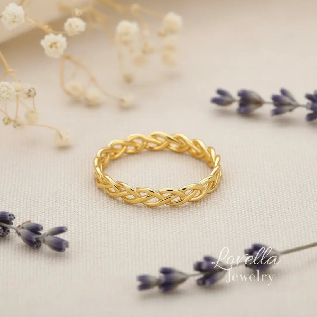 Gold-tone stainless steel braided ring in a flat lay photo with delicate flowers on a neutral background.