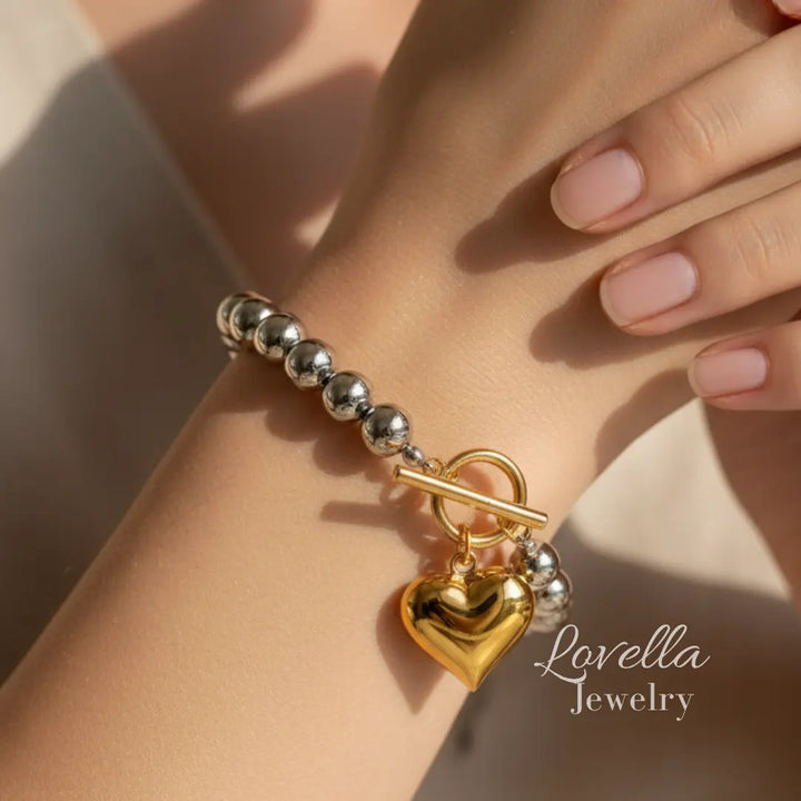 Bracelet with gold heart charm and silver beads on a wrist, Lovella Jewelry branding visible.