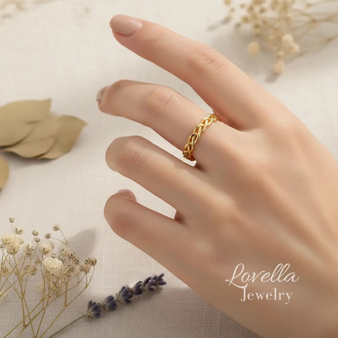 Model wearing a gold-tone stainless steel braided ring, shown on hand in soft natural light.