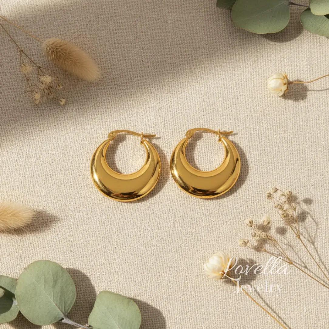 Gold hoop earrings on a textured surface with greenery