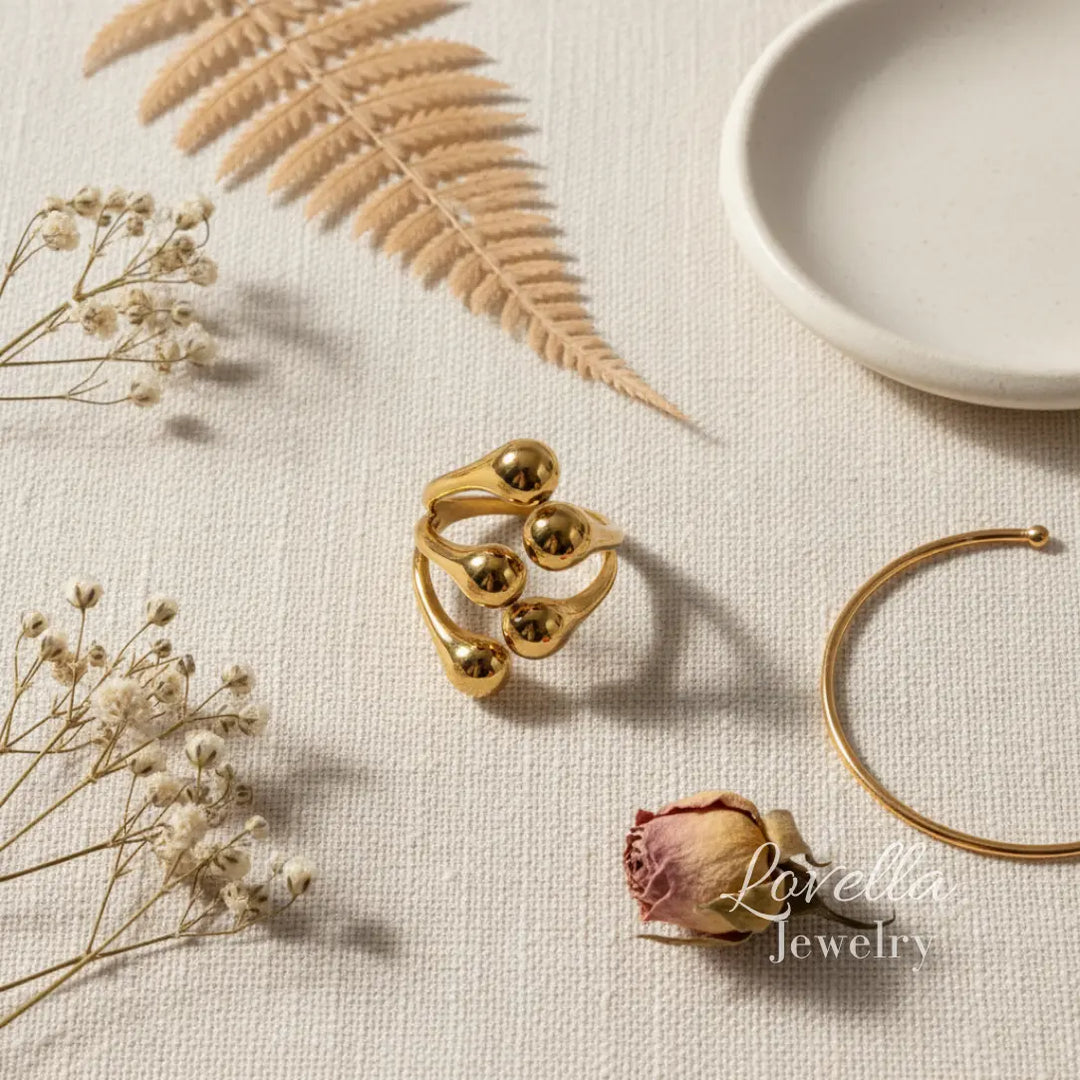 Gold ring and bracelet on a textured surface with dried flowers and leaves, Lovellia Jewelry branding visible.