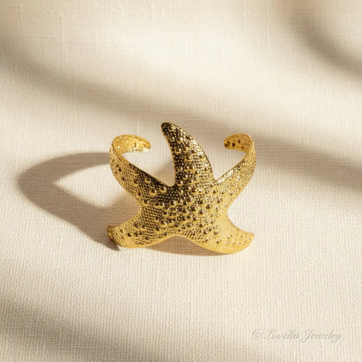 Gold starfish-shaped ring on a beige fabric background
