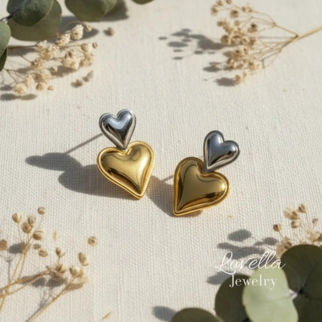 Heart-shaped earrings in gold and silver on a natural background with 'Lovella Jewelry' branding.