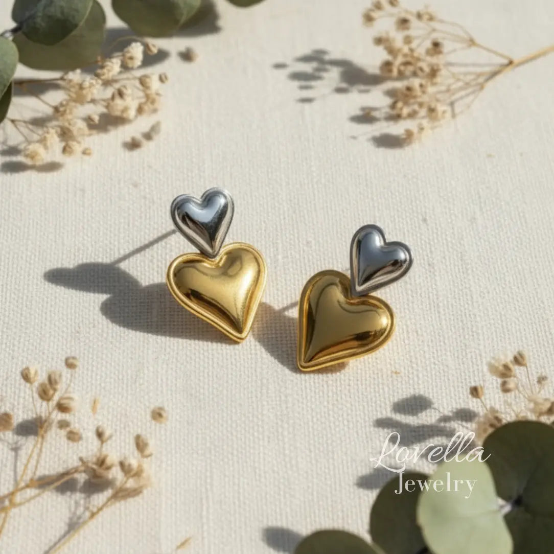 Heart-shaped earrings in gold and silver on a natural background with 'Lovella Jewelry' branding.