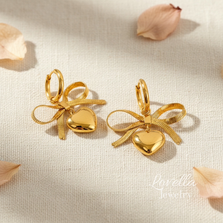 Gold heart-shaped earrings with bow details on a light fabric background