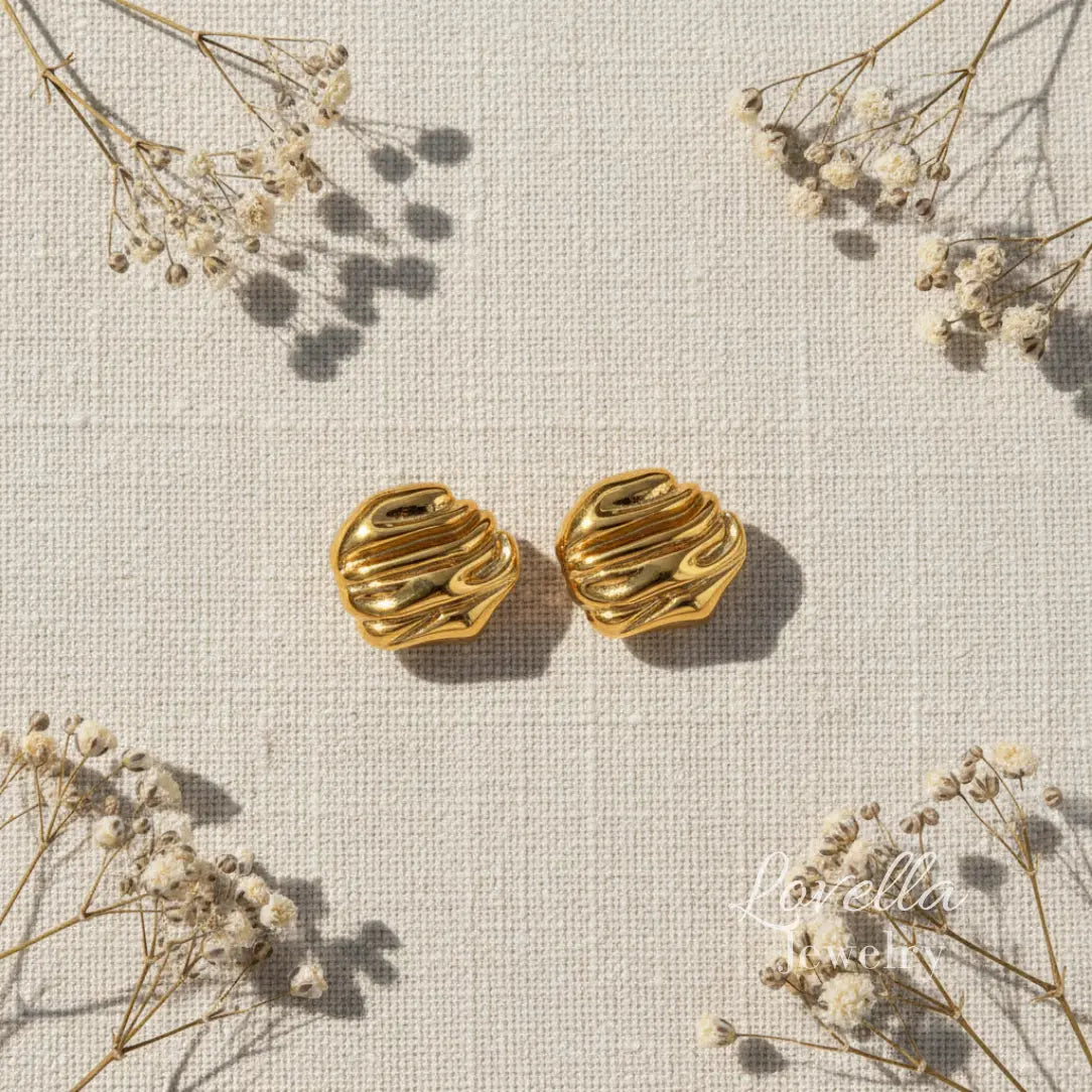 Gold chunky swirl stud earrings on cream linen background with dried flowers and Lovella Jewelry logo