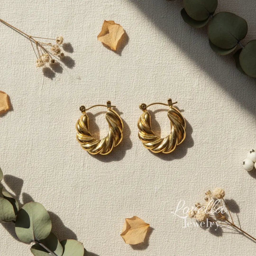 Gold hoop earrings on a textured surface with dried leaves and flowers.