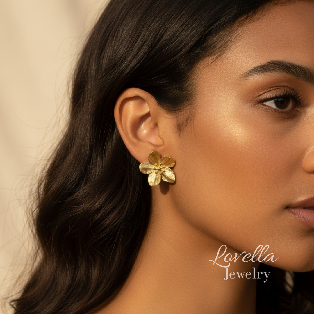 Close-up of a woman wearing gold flower earrings with 'Lovella Jewelry' branding.