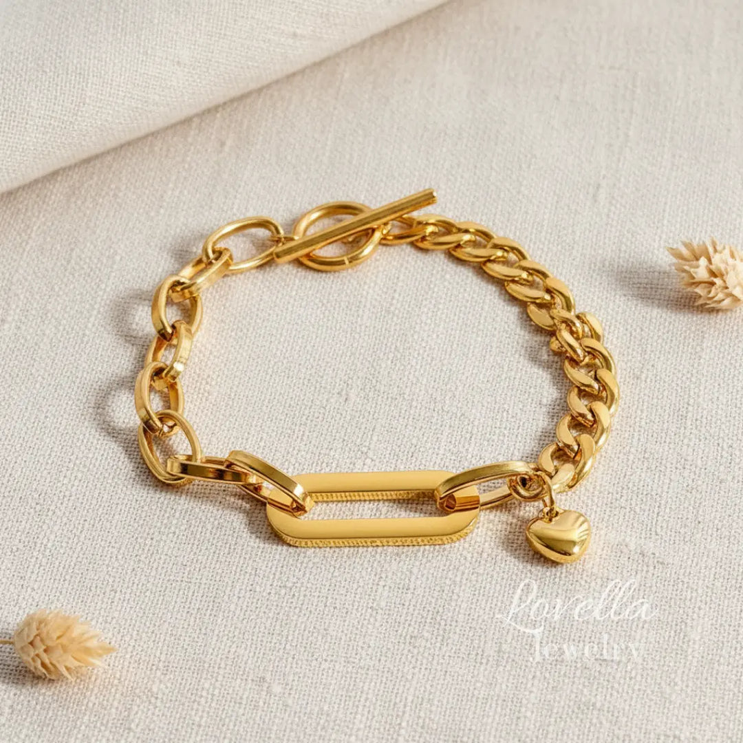 Gold chain bracelet with a heart charm on a light beige background