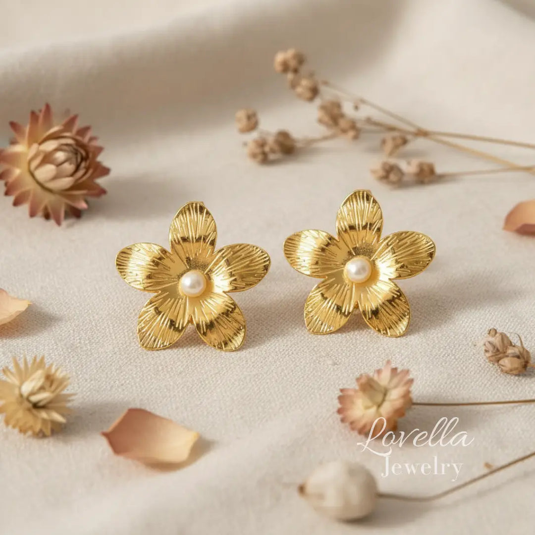 Gold flower-shaped earrings with pearl centers on a beige surface with dried flowers.