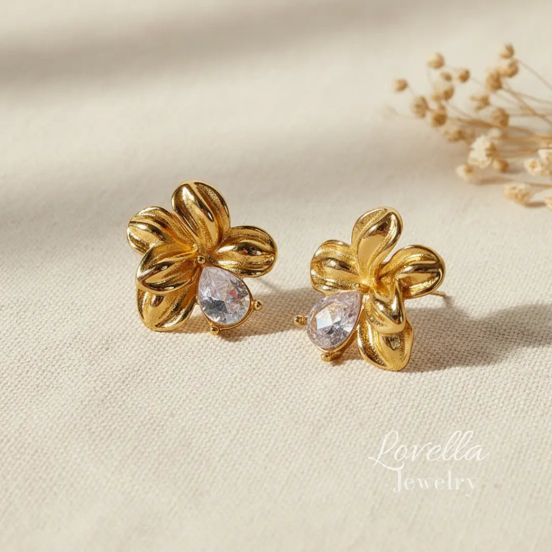 Gold floral earrings with clear stones on a beige background, branded 'Lovella'.