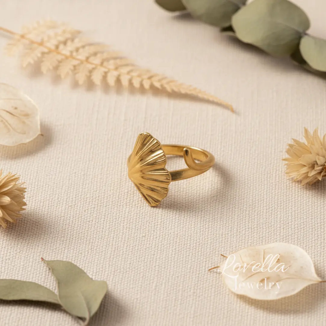Gold ring on a textured surface with dried flowers and leaves, featuring 'Lorella Jewelry' branding.