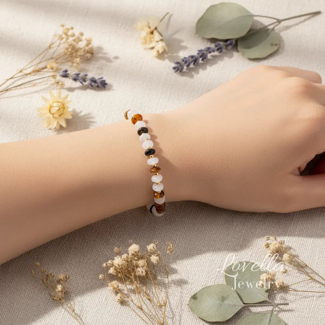 Natural stone bracelet on a wrist with dried flowers and leaves on a textured surface, Lovella Jewelry brand visible.