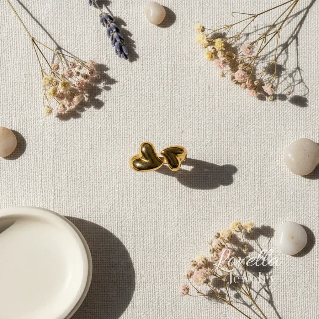 Gold heart-shaped earrings on a light surface with dried flowers and stones.