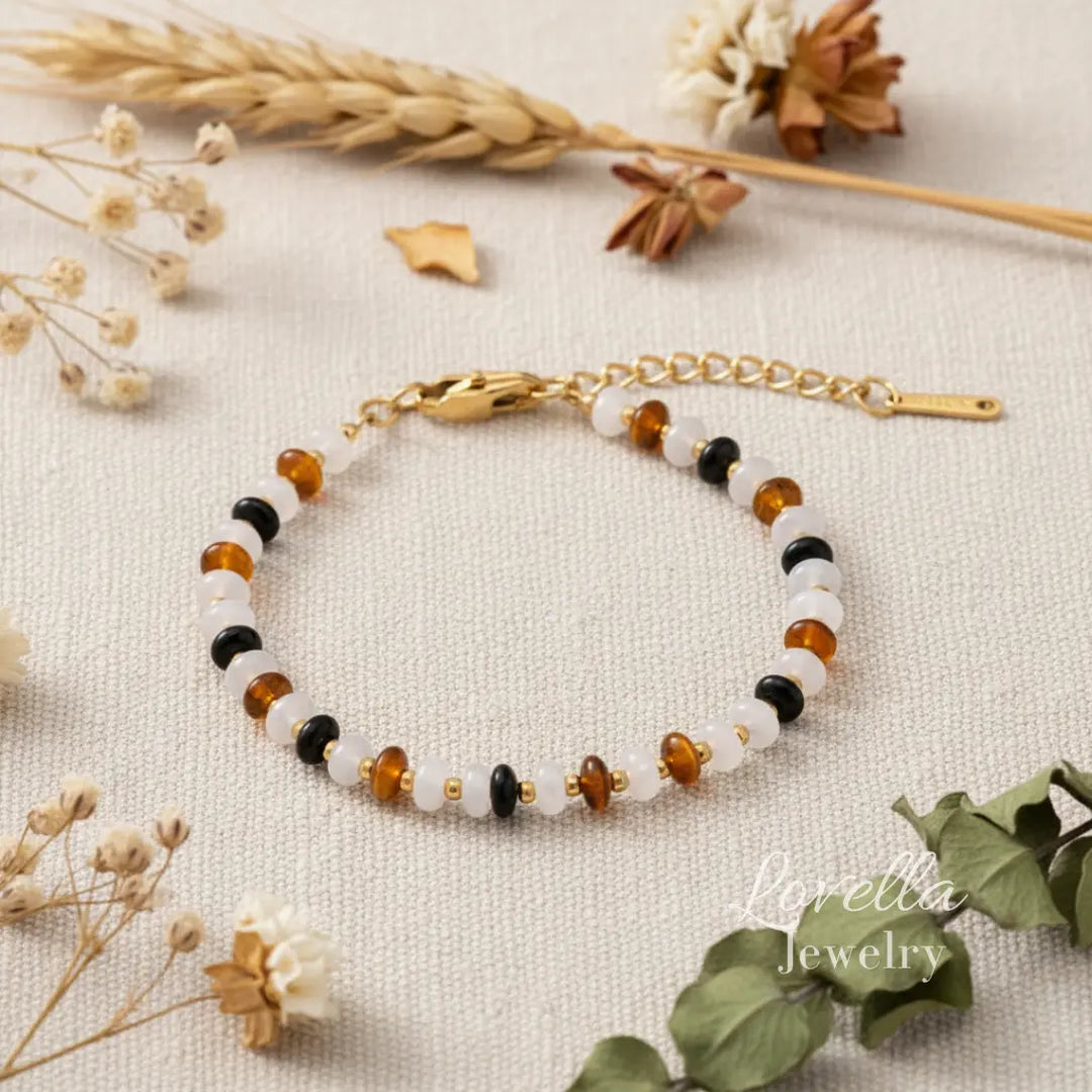 Natural stones bracelet with gold clasp on a textured surface with flowers and leaves.