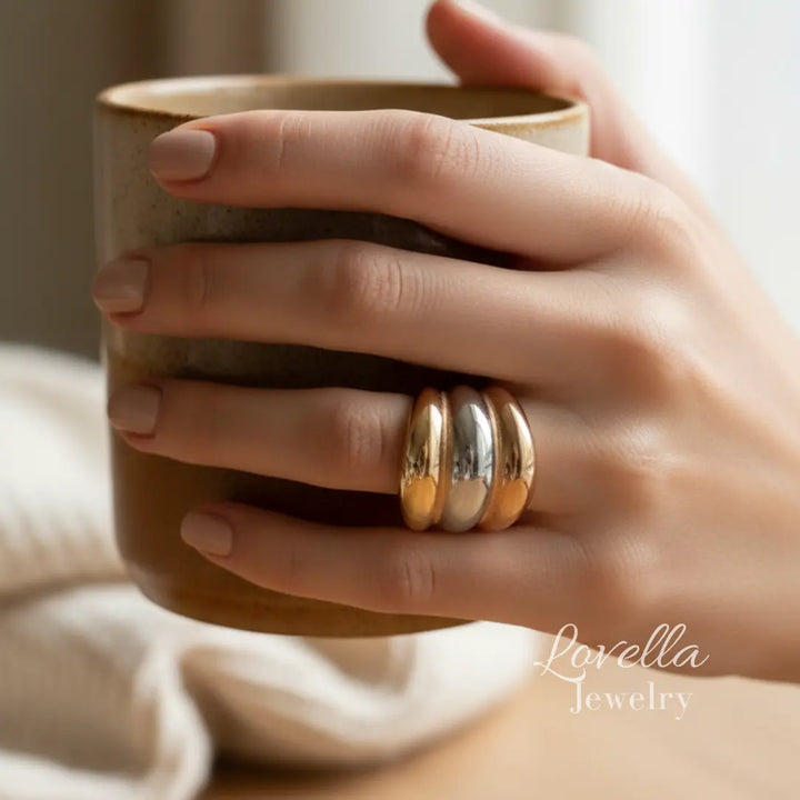 Hand holding a mug with three tone rings on a blurred background, featuring Lovella Jewelry.