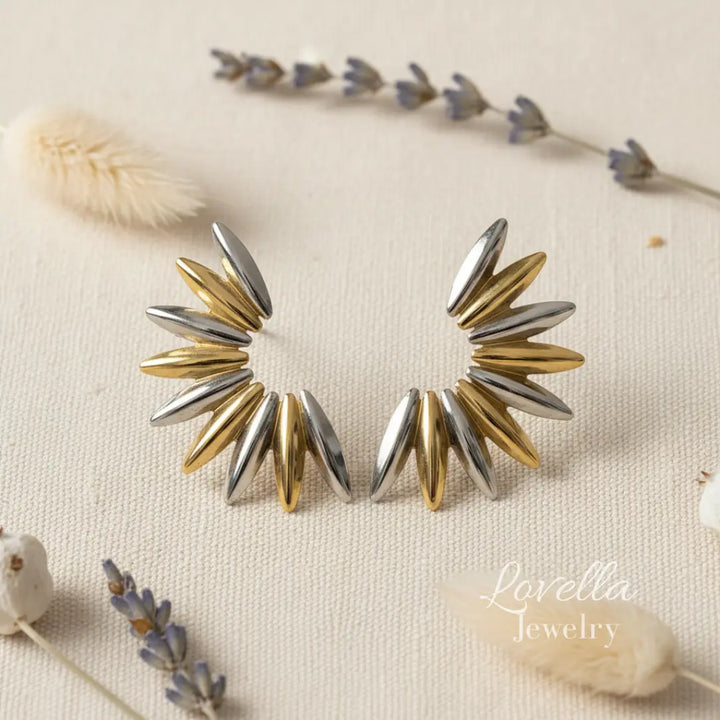 Pair of gold and silver spike earrings on a neutral background with floral elements.