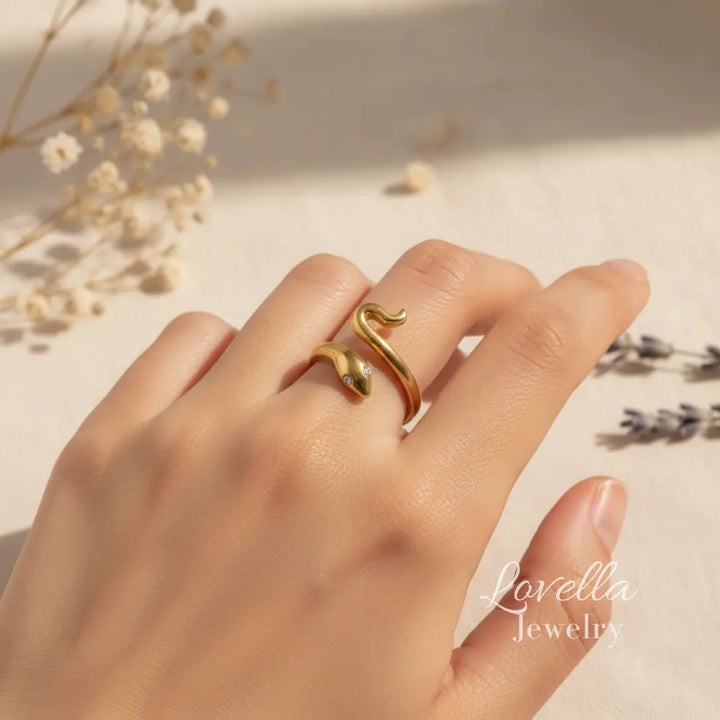 Gold ring on a hand with 'Lovellia Jewelry' branding, surrounded by dried flowers.