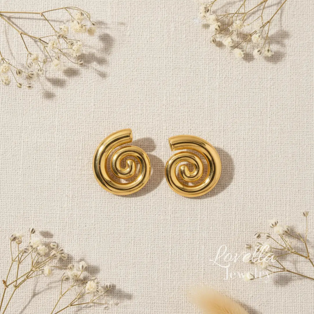 Gold spiral earrings on a textured beige background with delicate white flowers.
