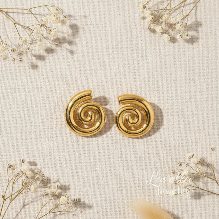 Gold spiral earrings on a textured beige background with delicate white flowers.
