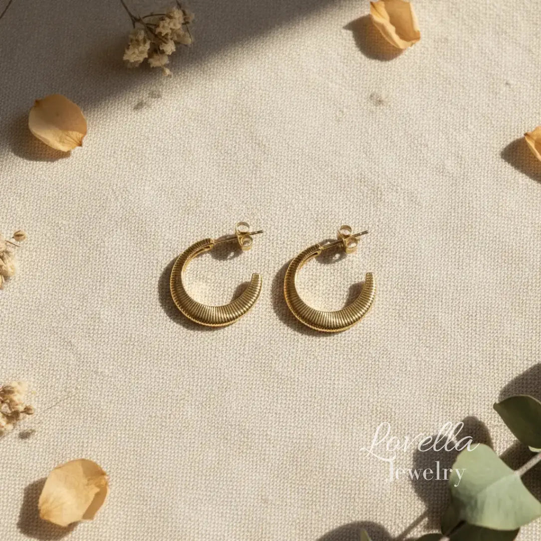 Gold hoop earrings on a textured beige surface with dried flowers and leaves.