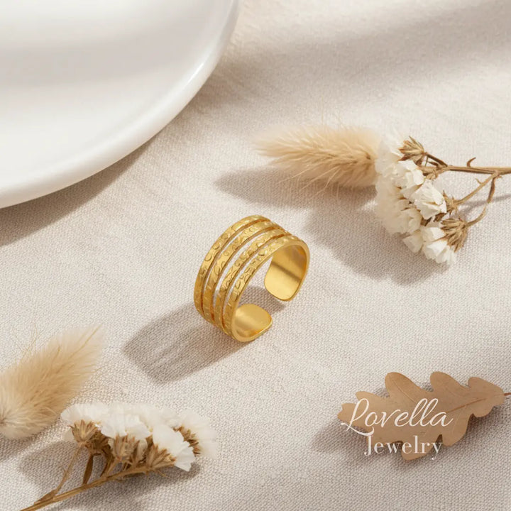 Gold ring on a textured surface with dried flowers and 'Lovella Jewelry' tag.