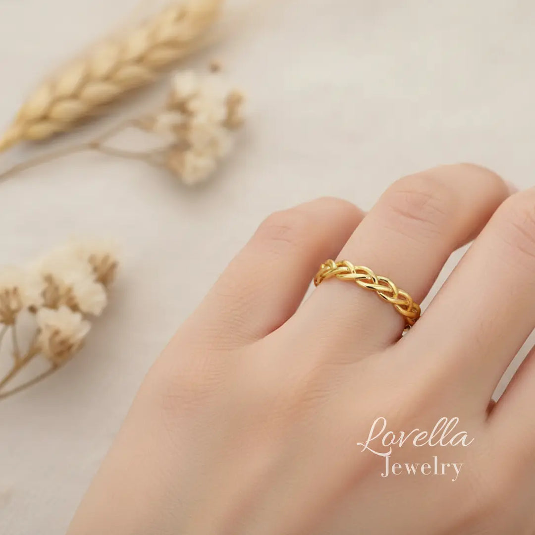 Model wearing a gold-tone stainless steel braided ring, shown on hand in soft natural light.