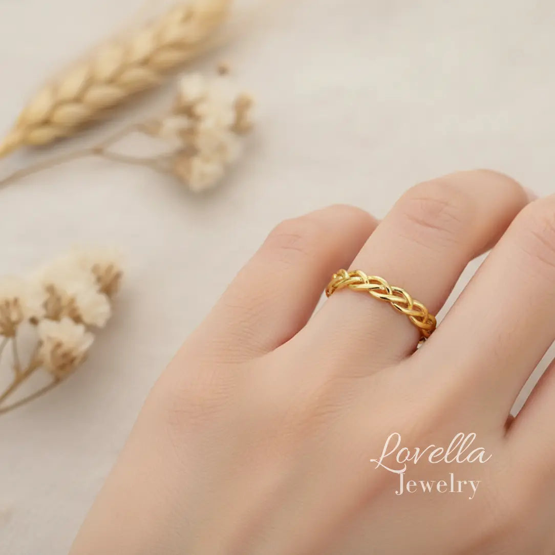 Model wearing a gold-tone stainless steel braided ring, shown on hand in soft natural light.