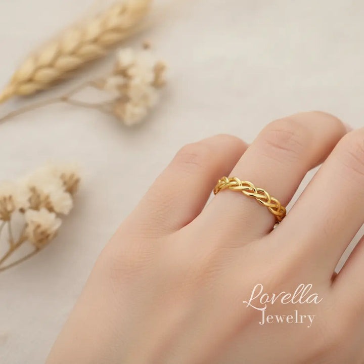 Model wearing a gold-tone stainless steel braided ring, shown on hand in soft natural light.