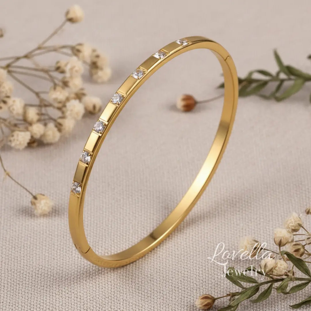 Gold bracelet with small diamonds on a beige fabric background with dried flowers.