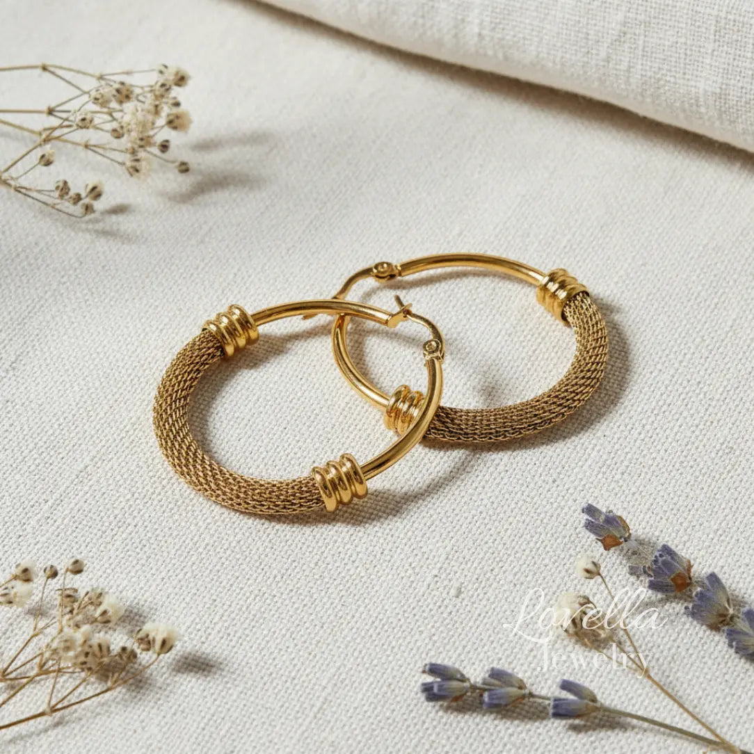 Gold hoop earrings on a light fabric background with dried flowers.