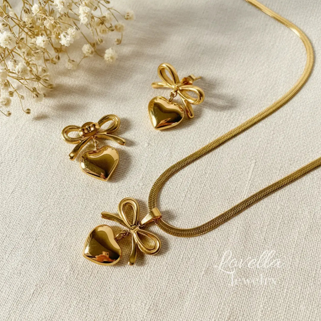 Gold heart-shaped jewelry set with bow details on a light fabric background.